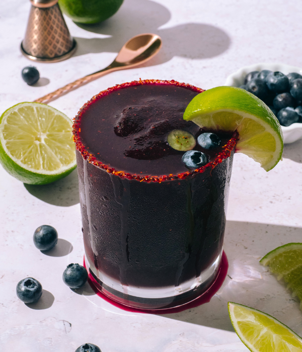Frozen blueberry Moon Juice Margarita presented in a short glass with slice of lime and blueberries. 
