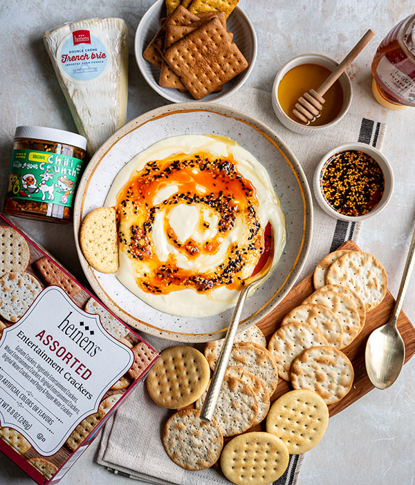 Sweet and Savory Whipped Brie in a Bowl with Chili Crunch and Crackers and Ingredients Surrounding