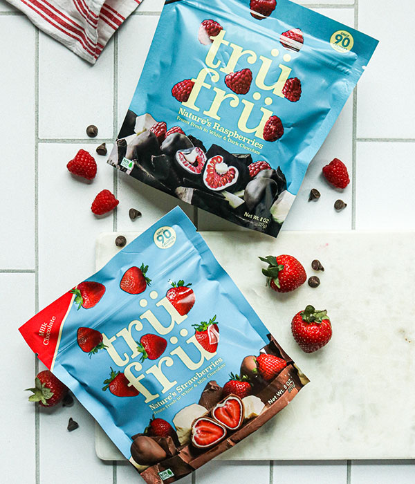 TruFru Frozen Chocolate Covered Fruit in Packaging on a Tile Surface with Fresh Berries Scattered Around Packaging