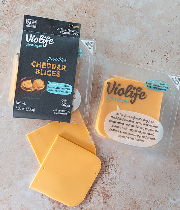 Violife Cheddar Slice Package and Fresh Cheddar Slices on a Neutral Surface