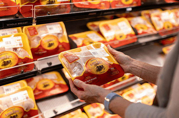 Customer Hands Holding a Package of Gerber's CARE Certified Chicken in Front of the Chicken Display at Heinen's 