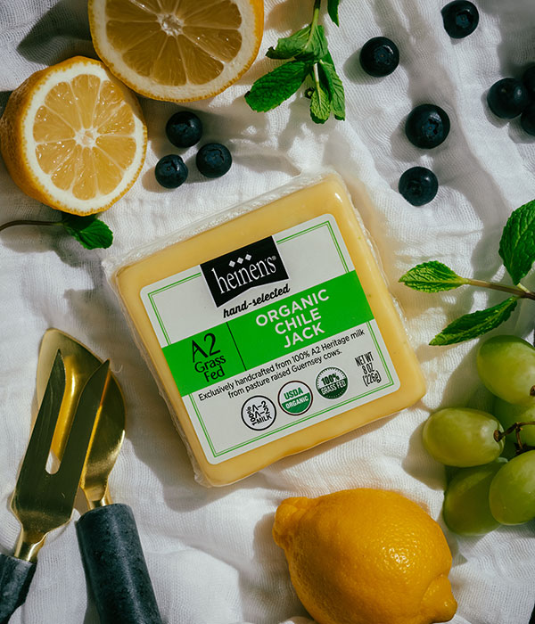 Heinen's Hand-Selected A2 Organic Chile Jack Cheese on a White Serving Cloth with Fresh Lemons, Fresh Blueberries, Fresh Herbs, Green Grapes and Cheese Servingware
