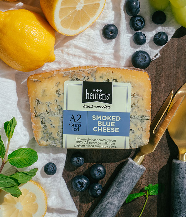 Heinen's Hand-Selected A2 Organic Smoked Blue Cheese on a White Serving Cloth and Serving Board with Fresh Lemons, Fresh Blueberries, Fresh Herbs and Cheese Servingware