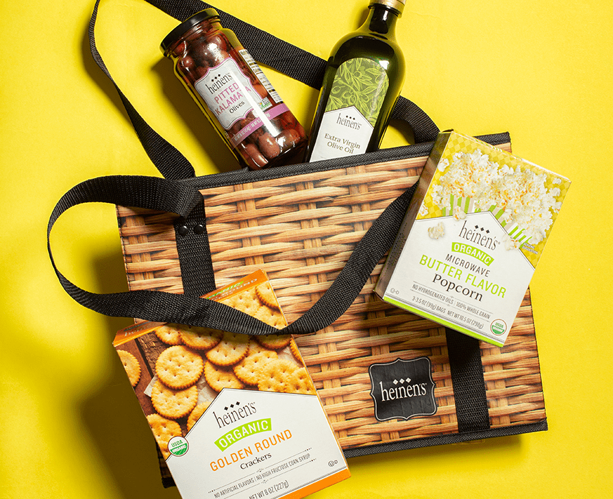 A Heinen's Box Toe Bag on a Vibrant Yellow Background. Shelf Stable Heinen's Brand Products are inside and outside of the bag,