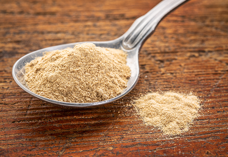 Maca Powder on a Silver Spoon on a Wooden Surface