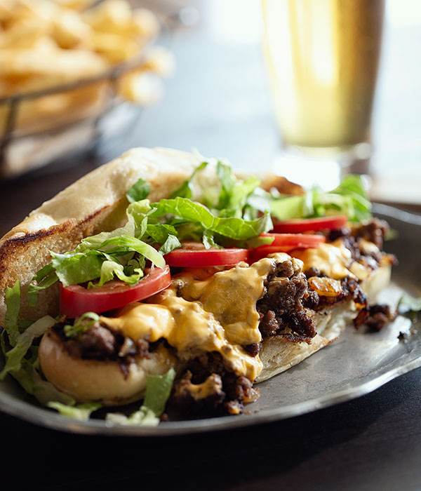 Vertical Image of an NYC Chopped Cheese Sandwich on a Plate with a Glass of Beer and a Basket of French Fries