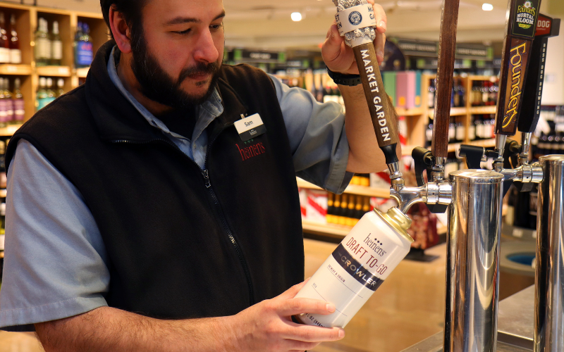 Heinen's Beer and Wine associate pouring beer from draft into Draft to Go Crowler